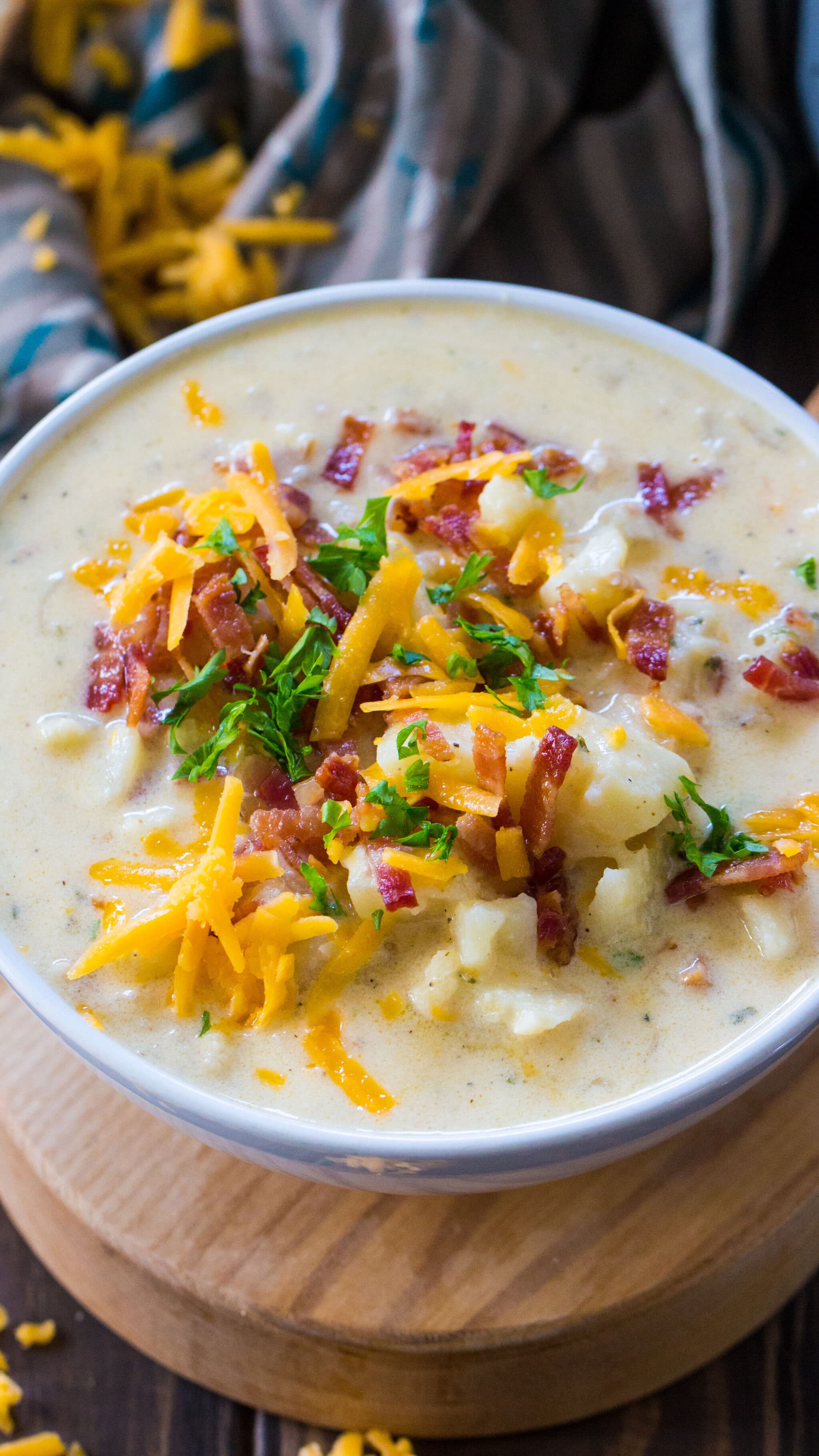 A steaming bowl of thick potato soup garnished with shredded cheese and crispy bacon bits.